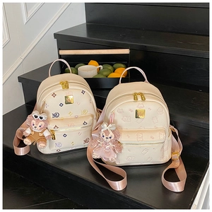 Detail of beige backpacks with embossed patterns and plush charms on wooden stairs