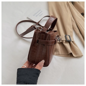 Detailed view of brown crocodile texture mini bag with silver buckle on neutral fabric