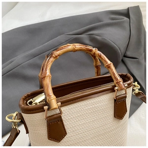 Detailed view of woven bucket bag with bamboo handle and brown leather trim details
