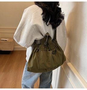 Detail of olive green nylon tote bag showing drawstring closure and side D-ring metal hook