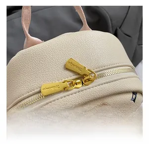 Close-up of golden dual zippers and textured lychee leather on a beige backpack
