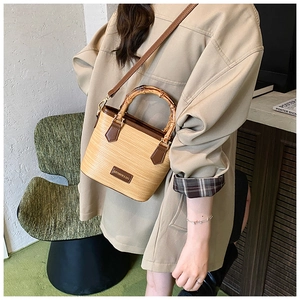 Detailed view of a woven bucket bag with bamboo handle and brown leather straps
