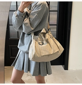 Detail of beige nylon tote bag featuring drawstring pleats and metal D-ring buckle