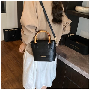 Detail of black woven bucket bag with bamboo handle and golden hardware on shoulder
