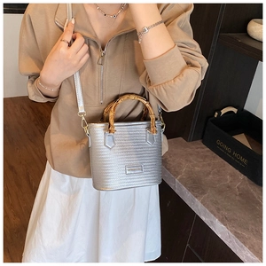 Detailed shot of silver woven handbag featuring natural bamboo handle and metal logo plaque