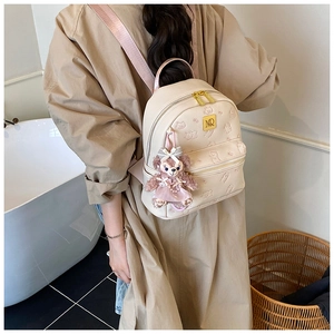Detail view of beige leather backpack featuring embossed bear pattern and plush fox charm