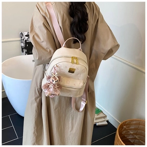 Close-up of cream textured leather backpack with pink cartoon bear prints and plush charm
