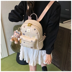 Close-up of cream mini backpack with colorful monogram embroidery and pink bear charm