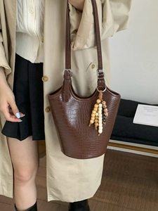 Brown crocodile pattern bucket tote bag with decorative beaded tassel on beige trench coat