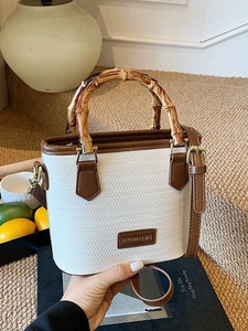 Chic off-white woven bucket bag with bamboo top handle and brown leather shoulder strap