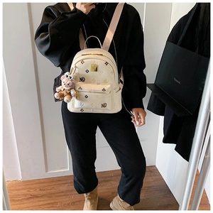 Detail of cream backpack with MQ pattern, pink straps and plush charm on female model