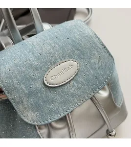 Gros plan du sac à dos en denim bleu et argent avec détails cloutés et logo de marque