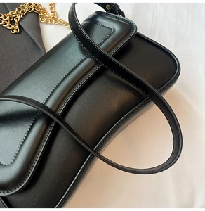 Détail du sac sous le bras en cuir noir minimaliste avec coutures et chaîne dorée