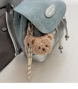 Détail d'un sac à dos en denim bleu clair avec strass et un charm d'ours en peluche brun