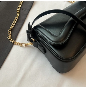 Gros plan d'un sac à bandoulière en cuir noir avec chaîne dorée et bordure surpiquée