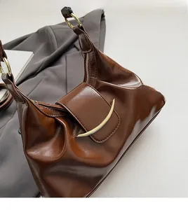 Detail view of brown glossy leather crossbody bag with elegant gold hardware accents