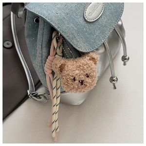Détail du sac à dos en jean avec rivets argentés, logo en métal et breloque ourson