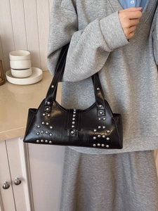 Chic black PU leather tote with silver rivets held by a model in a cozy indoor setting