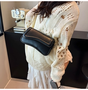Sac à bandoulière noir minimaliste avec chaîne dorée porté par un mannequin au café