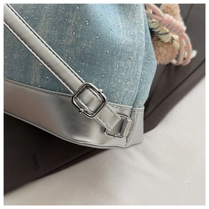 Détail d'un sac à dos en denim bleu clair avec clous argentés et boucle métallique