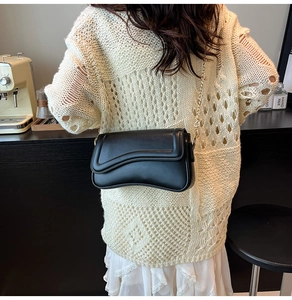Détail du sac bandoulière en cuir noir avec rabat ondulé et chaîne dorée