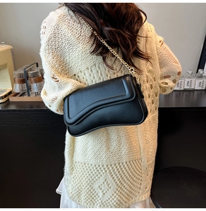 Détail du sac bandoulière en cuir noir avec chaîne dorée et design à rabat ondulé