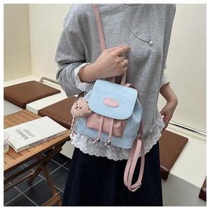 Détail d'un mini sac à dos bicolore avec breloque ours en peluche et logo de marque