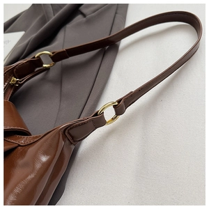 Detail of brown glossy leather bag with gold ring hardware and fine shoulder strap stitching