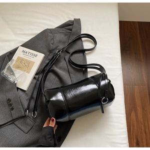 Detail einer schwarzen Lackleder-Zylindertasche auf grauem Blazer mit modernen Requisiten