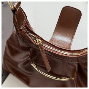 Detailed close-up of dark brown glossy PU leather bag with gold hardware and ruched design