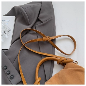 Detail of tan suede shoulder bag with adjustable strap and knotted handle on a grey blazer