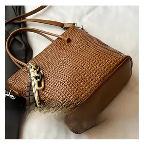 Detail of brown woven bucket bag with metal hardware and decorative ribbon charm