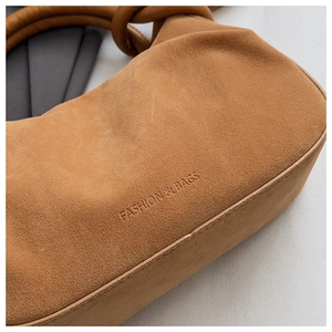 Detail of suede crossbody bag showing the fashion logo engraving and knotted handle