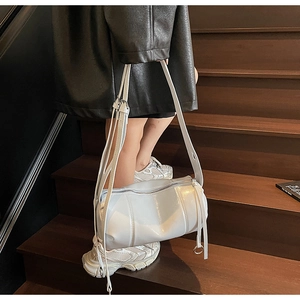 Detailsicht der weißen glänzenden Zylindertasche mit dekorativen Fransen und Metallschnallen