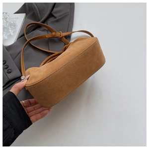 Close-up of brown suede shoulder bag showing the embossed logo and quality stitching