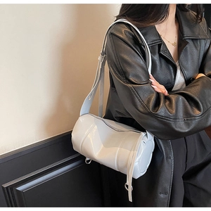 Detail einer weißen glänzenden Zylindertasche mit verstellbarem Riemen auf schwarzer Jacke