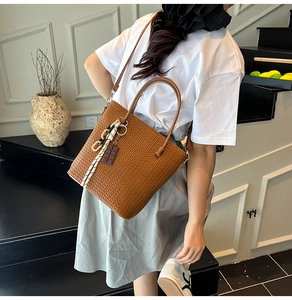 Brown woven tote bag with a patterned scarf and chocolate charm shown on a model