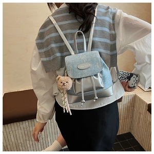 Détail d'un mini sac à dos en denim bleu clair avec rabat pailleté et breloque petit ours