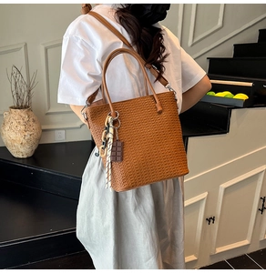Detail of a brown woven bucket bag with adjustable leather strap and trendy chocolate charm