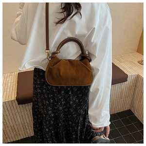 Detail of a brown suede cloud bag showing the round leather handle and soft gathered texture