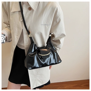Detail of black pleated leather crossbody bag worn with a classic cream trench coat