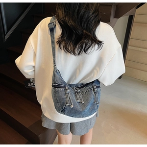 Détail du sac croissant en jean bleu avec poches zippées et nœuds sur la bandoulière
