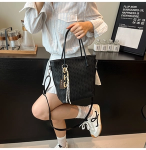 Detail of black woven bucket bag with leather handles and bohemian chain tassel charm