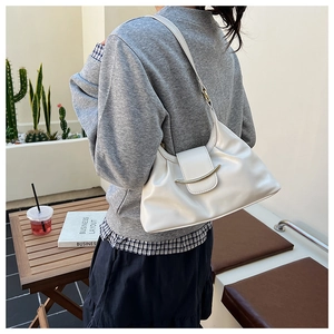 Detail of off-white pleated shoulder bag with gold metallic trim worn by a model