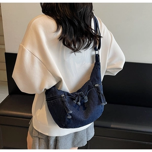 Détail du sac croissant en denim bleu foncé avec cordes et poches sur un sweat à capuche blanc