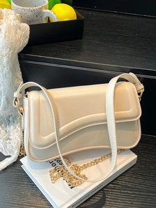 Sac bandoulière beige avec rabat ondulé et chaîne dorée sur livres et déco style