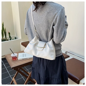 Detailed side view of a white crescent moon bag with golden hardware on a wooden table