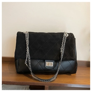 Detail of black quilted tote bag showing suede flap, metallic chain, and turn-lock closure