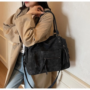 Dettaglio di una grande borsa tote in pelle scamosciata nera con tasche e nappine su trench