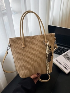 Large khaki woven bucket tote bag with round handles and adjustable strap in lifestyle setting